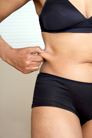 A torso of a woman grabbing exess fat from her waist